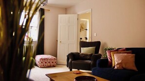 A living room with a sofa, a chair, a coffee table, and a door leading to another room. - Templar Mews, heart of town (Cirencester)