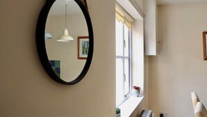 A room with a round mirror, a hanging pendant light, a window with a view, and a piano. - Templar Mews, heart of town (Cirencester)