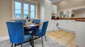A modern kitchen with white cabinets, a built-in washing machine, and a dining area with blue chairs and a round table. - Discounts for Extended Stays - sleeps 4 (Gloucestershire)
