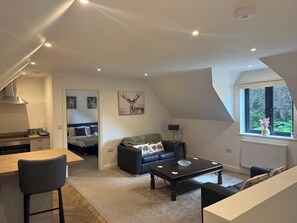 A compact living space with a kitchenette, a dining area, a sofa, a coffee table, and a window with a view. - The Carriage House, peaceful, beautiful cottage (Gloucestershire)