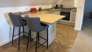 A modern kitchen with a wooden island, two bar stools, a red toaster, and a built-in oven.