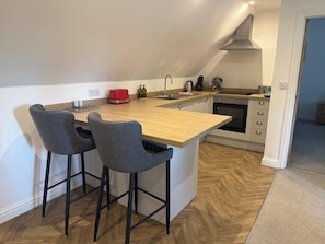 A modern kitchen with a wooden island, two bar stools, a red toaster, and a built-in oven. - The Carriage House, peaceful, beautiful cottage (Gloucestershire)