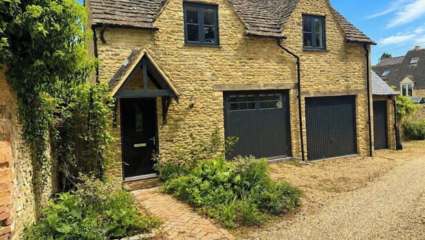 A stone house with a black door, two garage doors, and a gravel driveway.