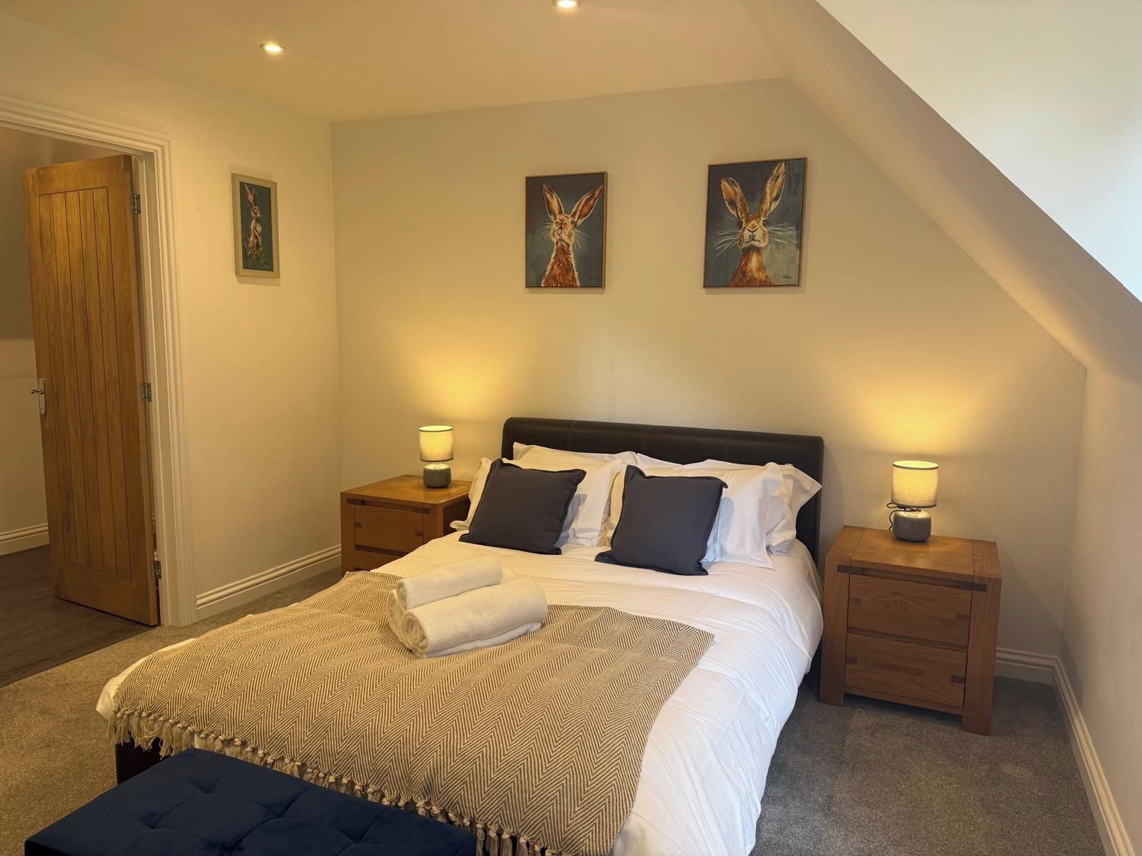 Ein Schlafzimmer mit einem Bett, zwei Nachttischen, einer Bank und zwei an der Wand befestigten Bildern.