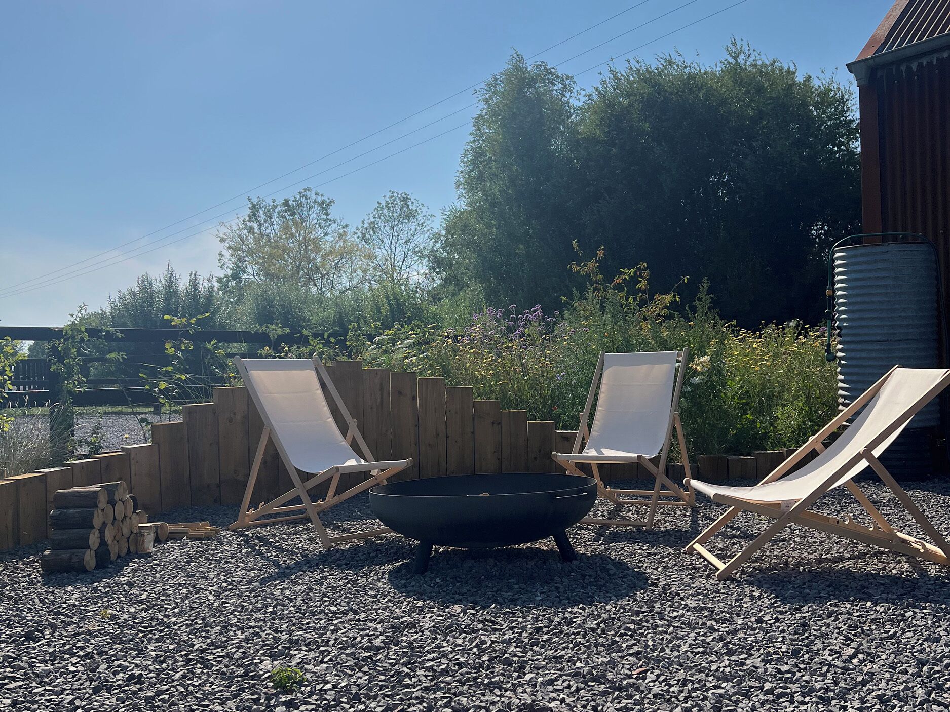 A gravel patio with two lounge chairs and a black fire pit.