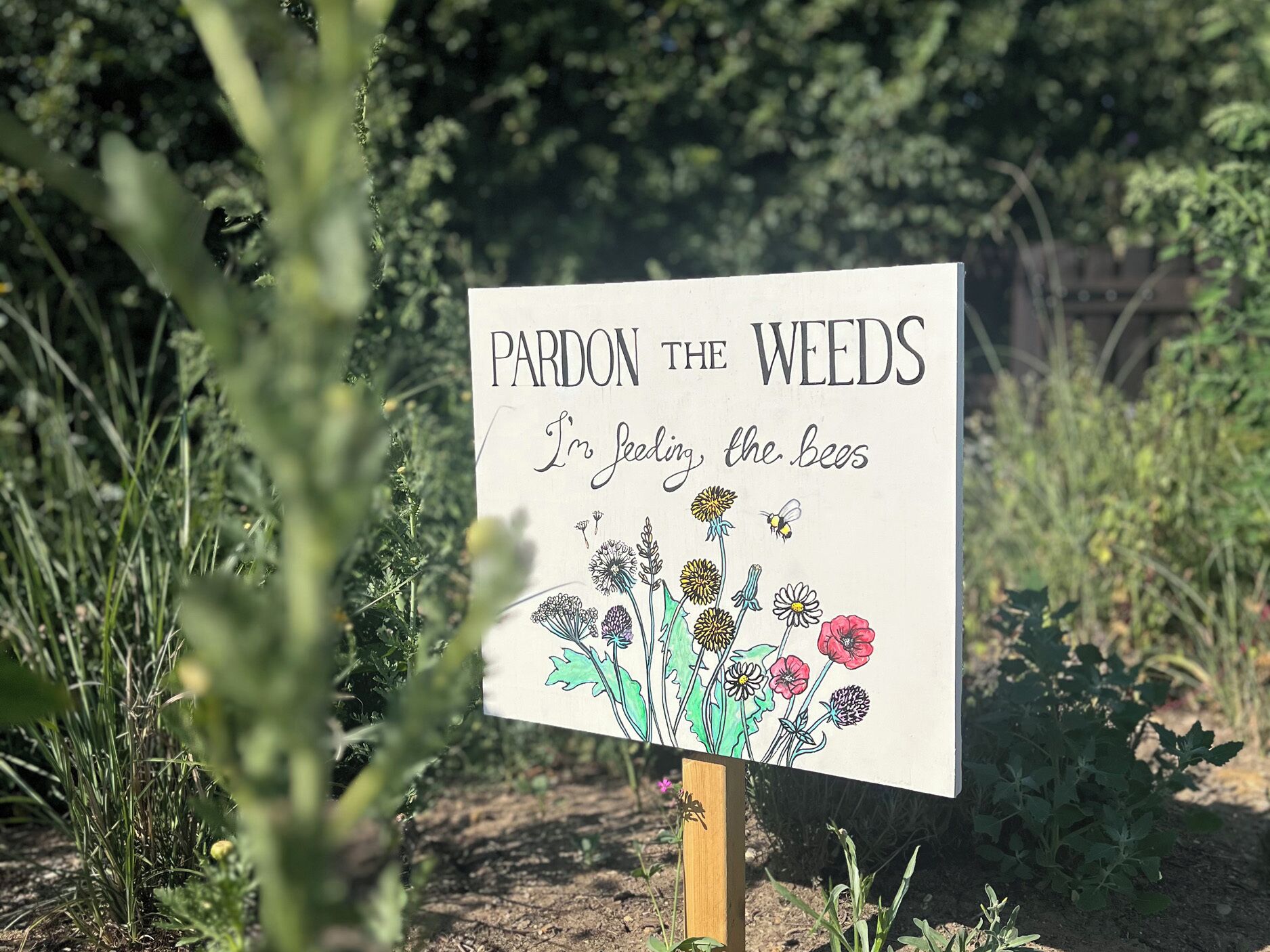 A sign with text and a drawing of flowers and bees, surrounded by greenery.