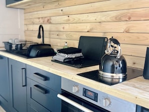 A kitchen with a wooden wall, a kettle, a kettle holder, a kettle warmer, and a digital oven control panel. - Rustwood Manor (Malmesbury)