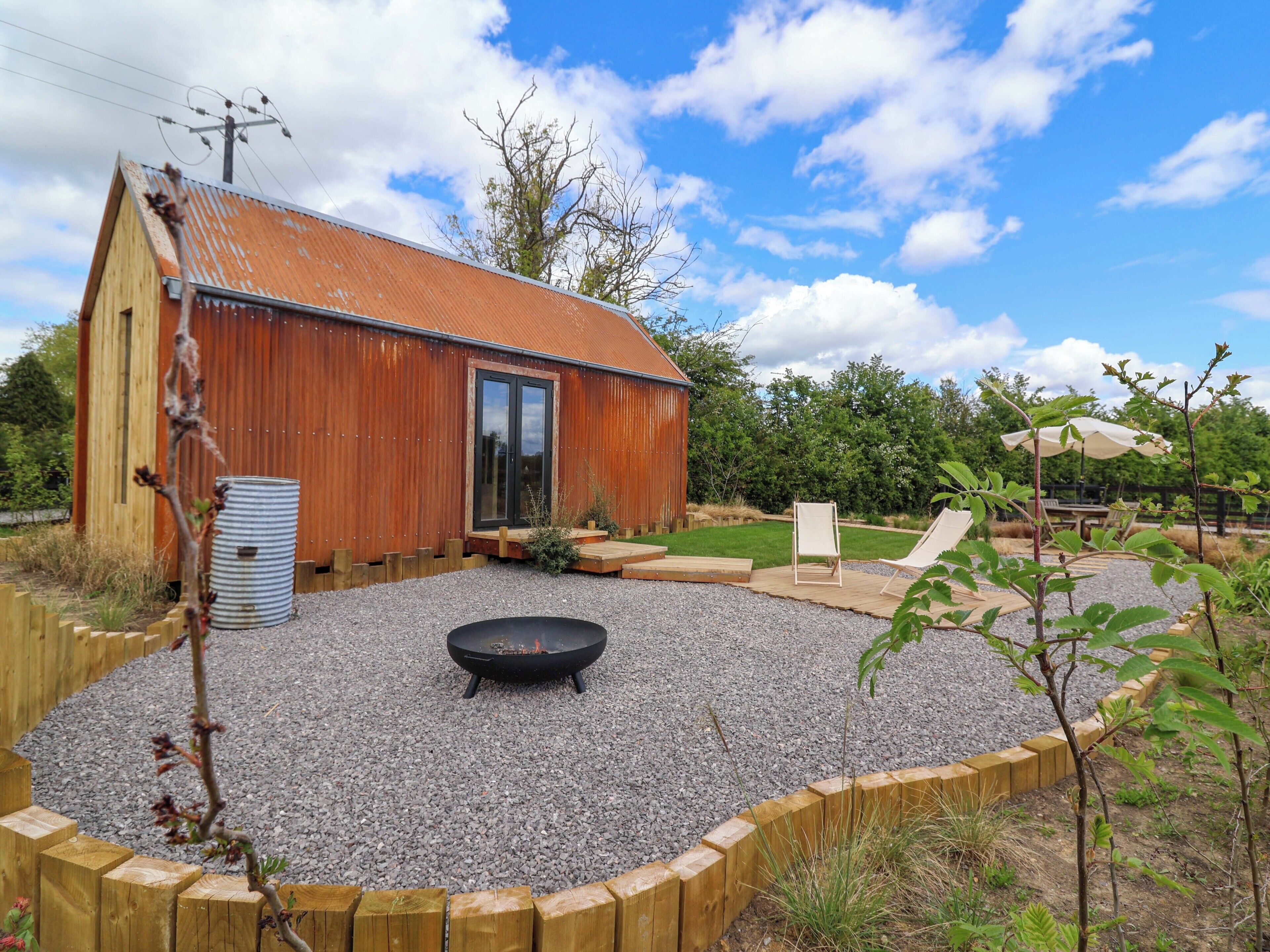 A rustic wooden building with a metal roof, a gravel patio, a black fire pit, and a wooden deck.