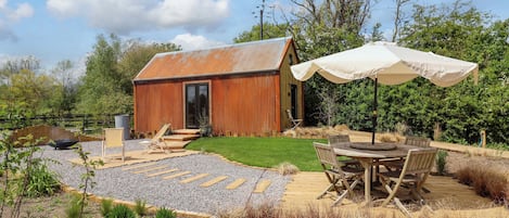 A rustic wooden cabin with a gravel patio, a wooden deck, and a table with chairs.