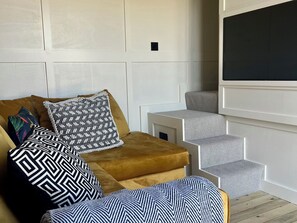 En moderne stue med en sofa, mønstrede hynder og en trappe op til en balkon.