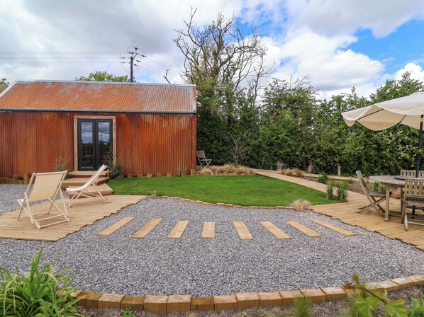 A rustic building with a metal roof, a gravel patio, and a wooden deck. - Rustwood Manor (Malmesbury)