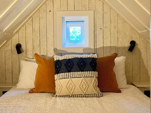 A bedroom with a sloped ceiling, a skylight, and a bed with three pillows. - Rustwood Manor (Malmesbury)