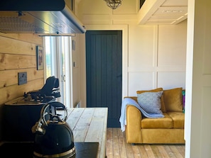 A cozy room with a wooden floor, a sofa with patterned cushions, a kettle, and a stove. - Rustwood Manor (Malmesbury)