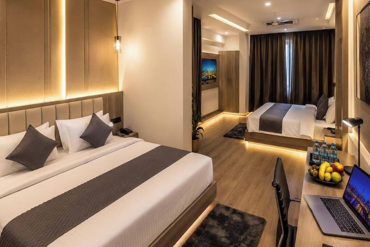Una habitación de hotel moderna con dos camas, un escritorio con una computadora portátil, un ventilador de techo y un televisor.