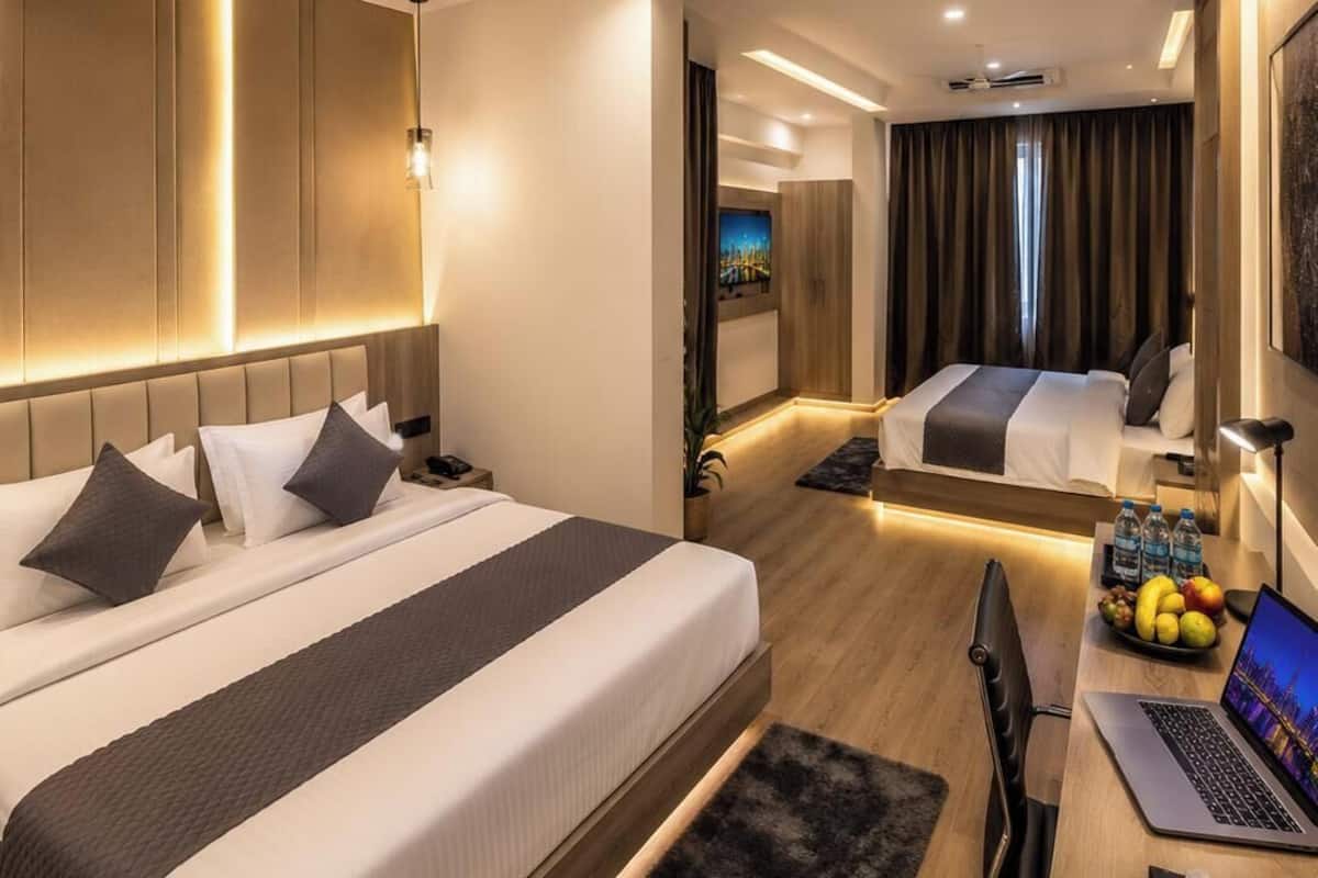 Ein modernes Hotelzimmer mit zwei Betten, einem Schreibtisch mit einem Laptop, einem Deckenventilator und einem Fernseher.