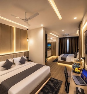 Una habitación de hotel moderna con dos camas, un escritorio con una computadora portátil, un ventilador de techo y un televisor.