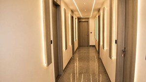 Un pasillo de hotel con puertas de madera, piso de mármol e iluminación empotrada.