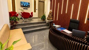 Un área de recepción moderna con un sofá, sillas rojas, un mostrador de recepción y una pantalla de televisión.
