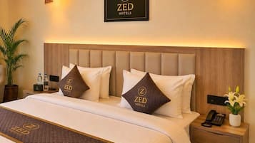 A hotel room with a bed, headboard, bedside tables, a nightstand, a potted plant, and a wall-mounted sign.