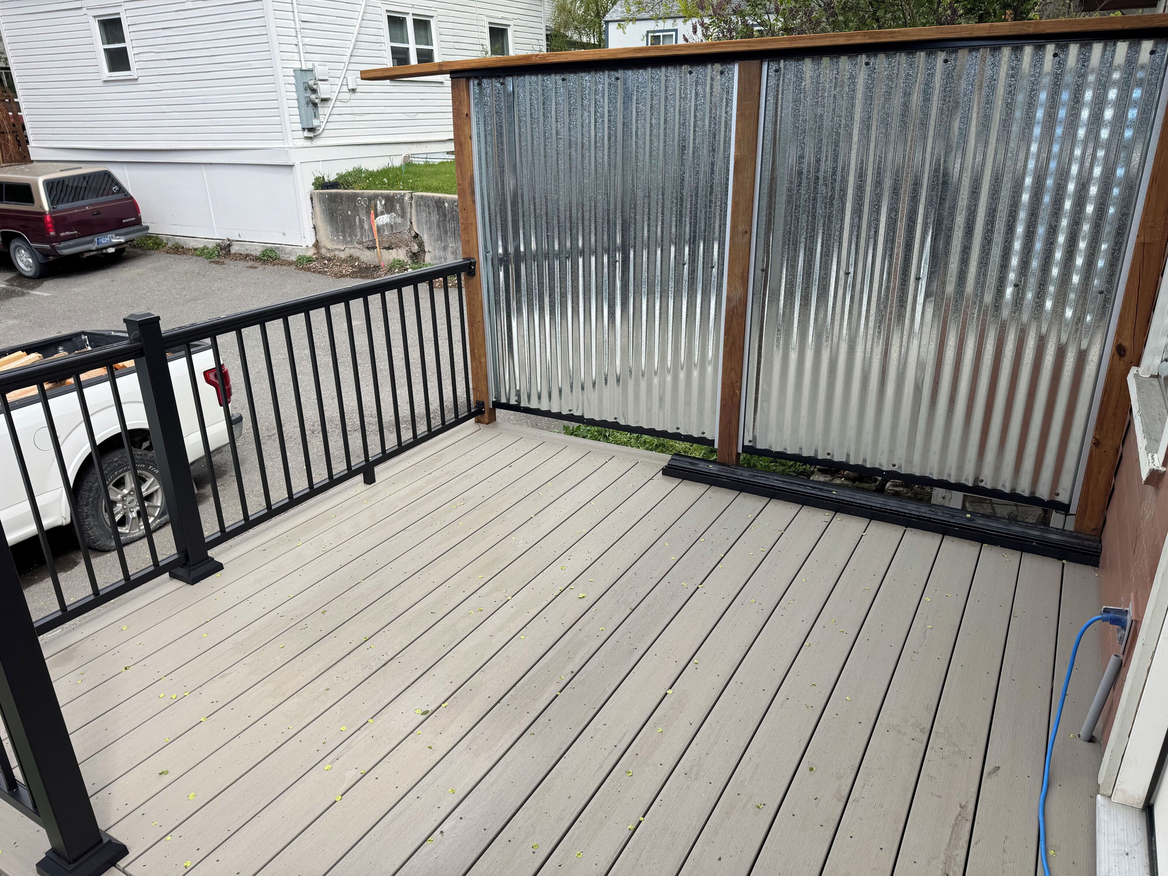 Eine Holzterrasse mit einem Metallzaun, ein geparktes Fahrzeug in der Nähe und ein Haus im Hintergrund.