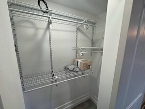Een inloopkast met metalen schapunits, een kledingroede en een klein opbergdoos.
