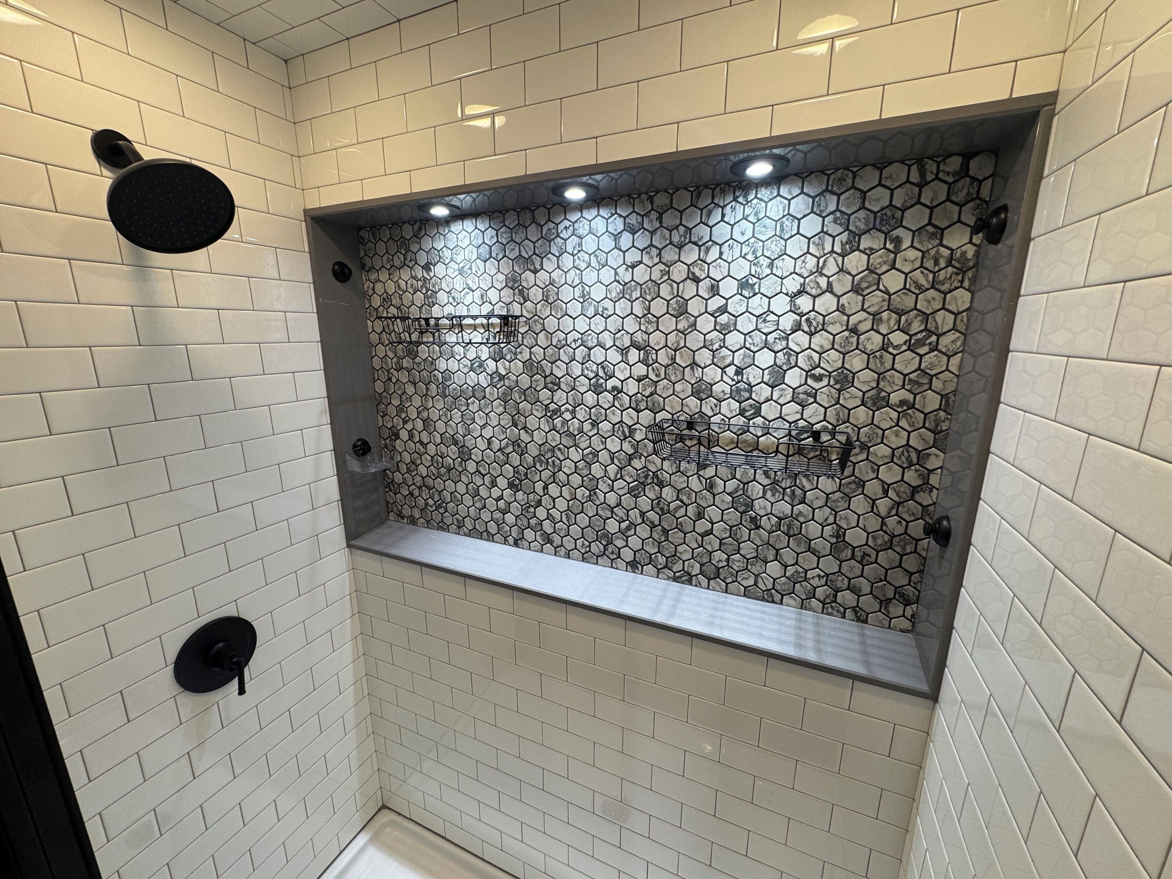Een douche met een betegeling in een honingraatpatroon, een bankje en een wandmengkraan.
