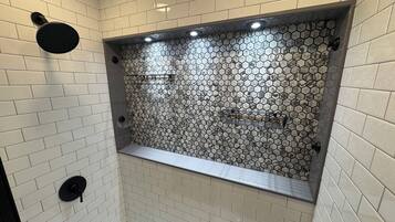 Een douche met een betegeling in een honingraatpatroon, een bankje en een wandmengkraan.
