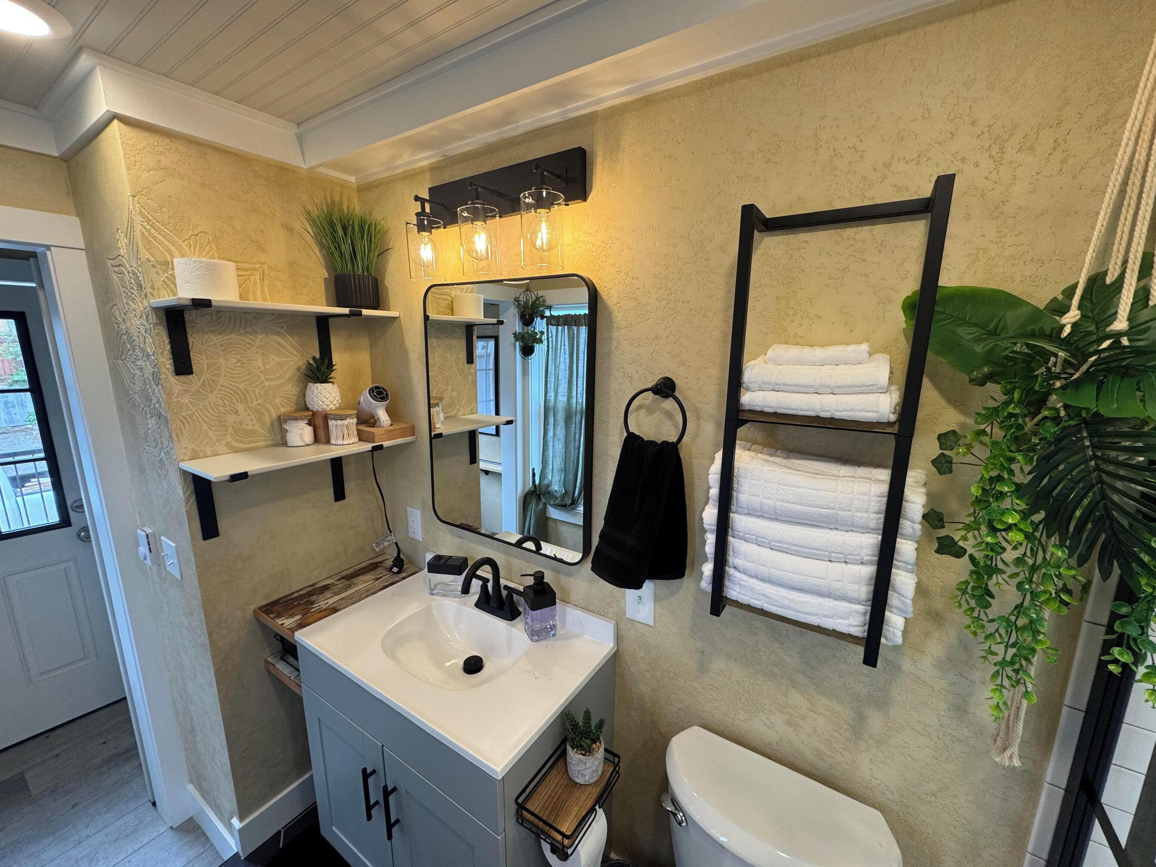 Een badkamer met een wastafel, spiegel, handdoekhouder, planken met toiletartikelen en een toilet.