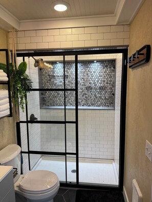 Een badkamer met een wit toilet, een douche met een glazen deur en een betegelde muur.