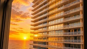 Een hoog gebouw met meerdere balkons, uitzicht op de ondergaande zon boven de oceaan, en een heldere lucht.