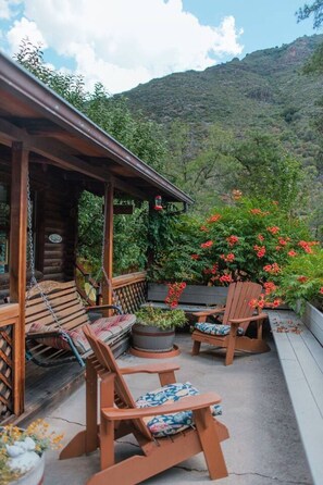 Une terrasse en bois dotée d’un espace salon couvert, d’un luminaire suspendu et offrant une vue sur un paysage montagneux.