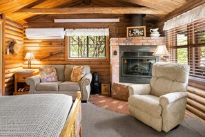 Interior acolhedor de uma cabana de madeira, com lareira, sofá, poltrona e cama.