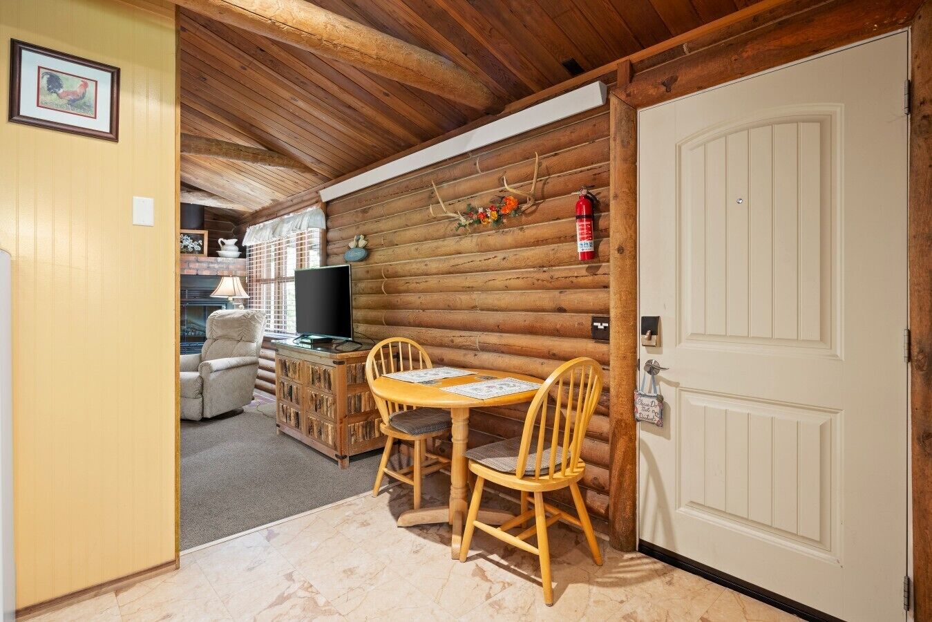 A log cabin interior with a dining area, a television, and a fireplace.