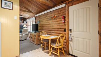 A log cabin interior with a dining area, a television, and a fireplace.