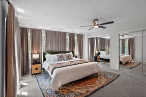 Een slaapkamer met een groot bed, een plafondventilator, een nachtkastje, een lamp en een spiegel.