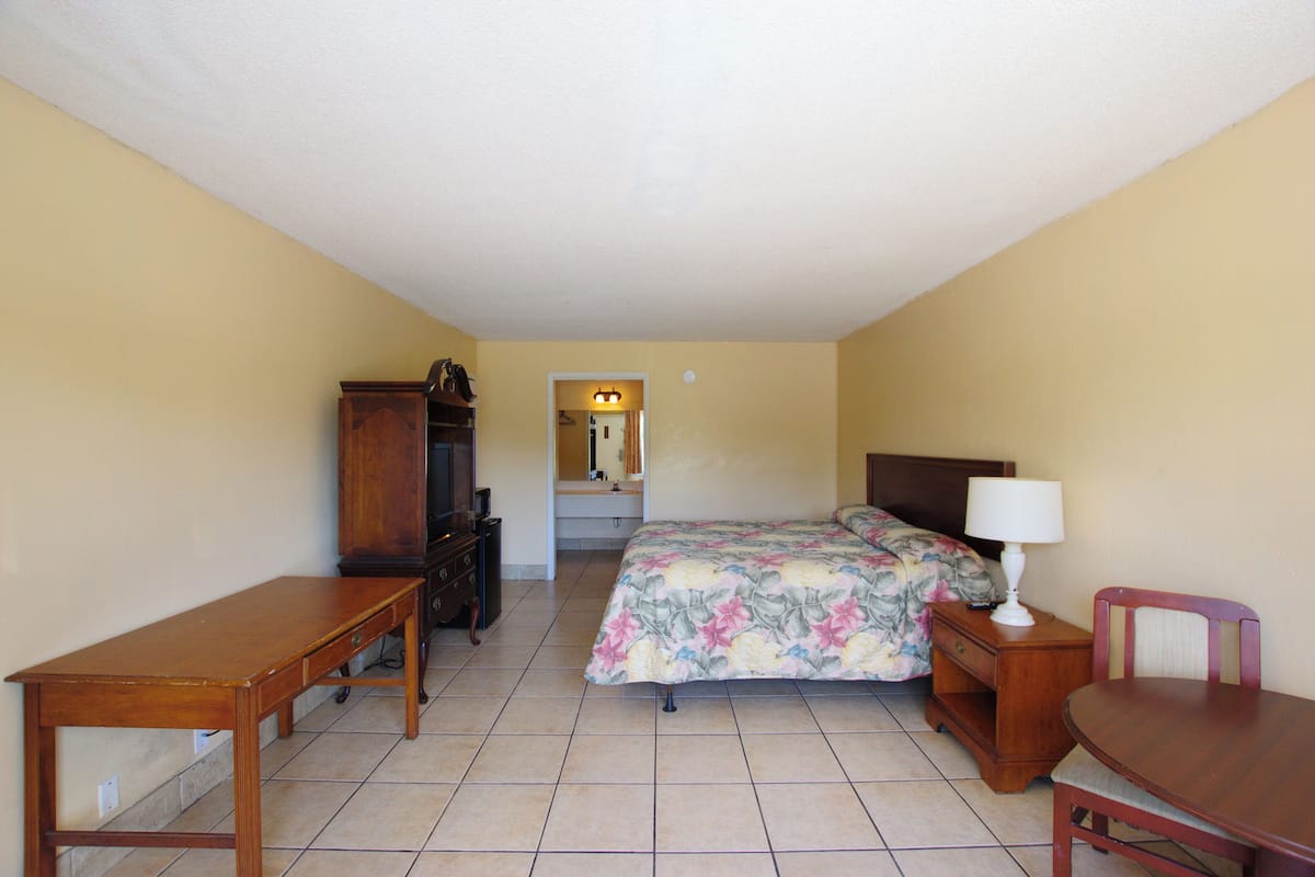 A hotel room with a bed, a desk, a chair, a nightstand, and a dresser.