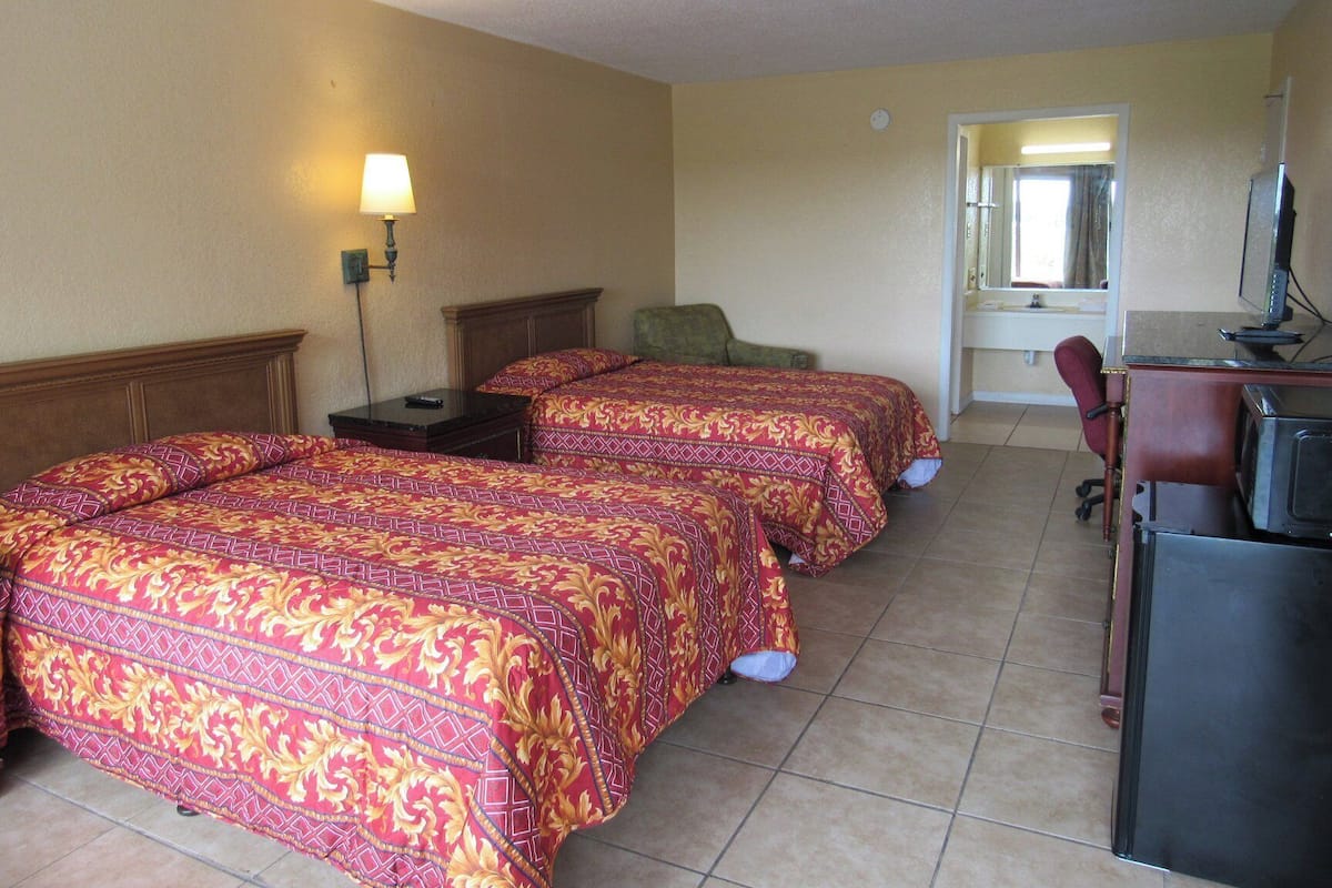 A hotel room with two beds, a desk, a chair, a lamp, and a window.