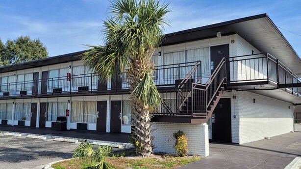 A motel with a two-story structure, a palm tree in the foreground, and a parking lot. - Paramount Lakeside Inn & Suites (Lakeland)