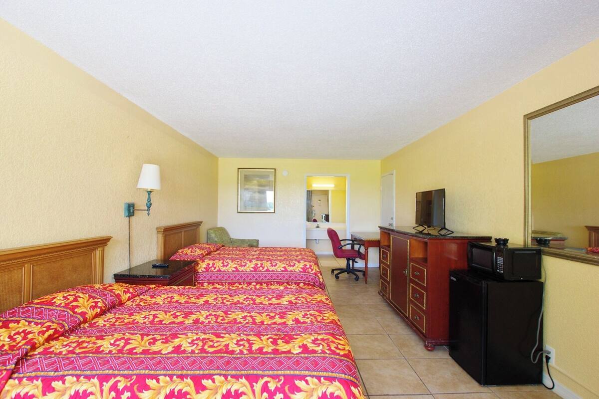 A hotel room with two beds, a desk, a chair, a television, and a minibar.