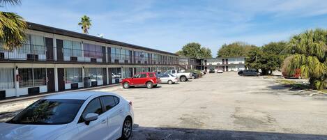 A motel with multiple-story buildings, a parking lot with several cars, and palm trees.