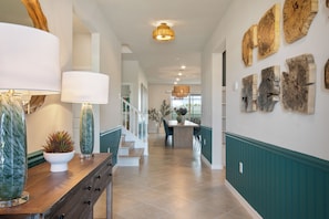 A hallway with a wooden bench, a white vase with a plant, and a wall-mounted wooden art piece.