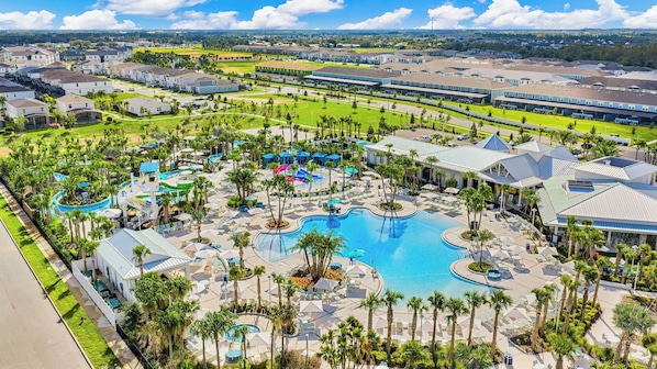 An aerial view of a resort with a large central pool, multiple smaller pools, and a water park area.
