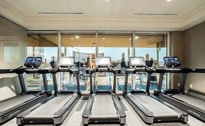 Ein Fitnessstudio mit Laufbändern und Trainingsgeräten, großen Fenstern und Blick auf einen Poolbereich.