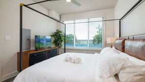 Ein Hotelzimmer mit Himmelbett, Flachbildfernseher, Topfpflanze und einem Fenster mit Jalousien.
