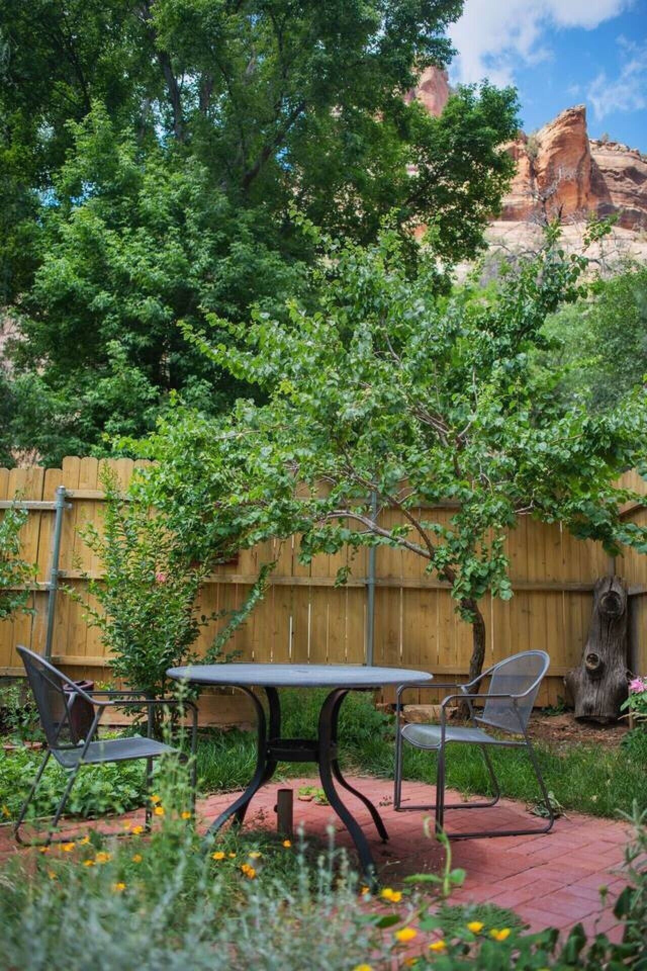 Een terras met een tafel en stoelen, omgeven door groen en een houten hek.