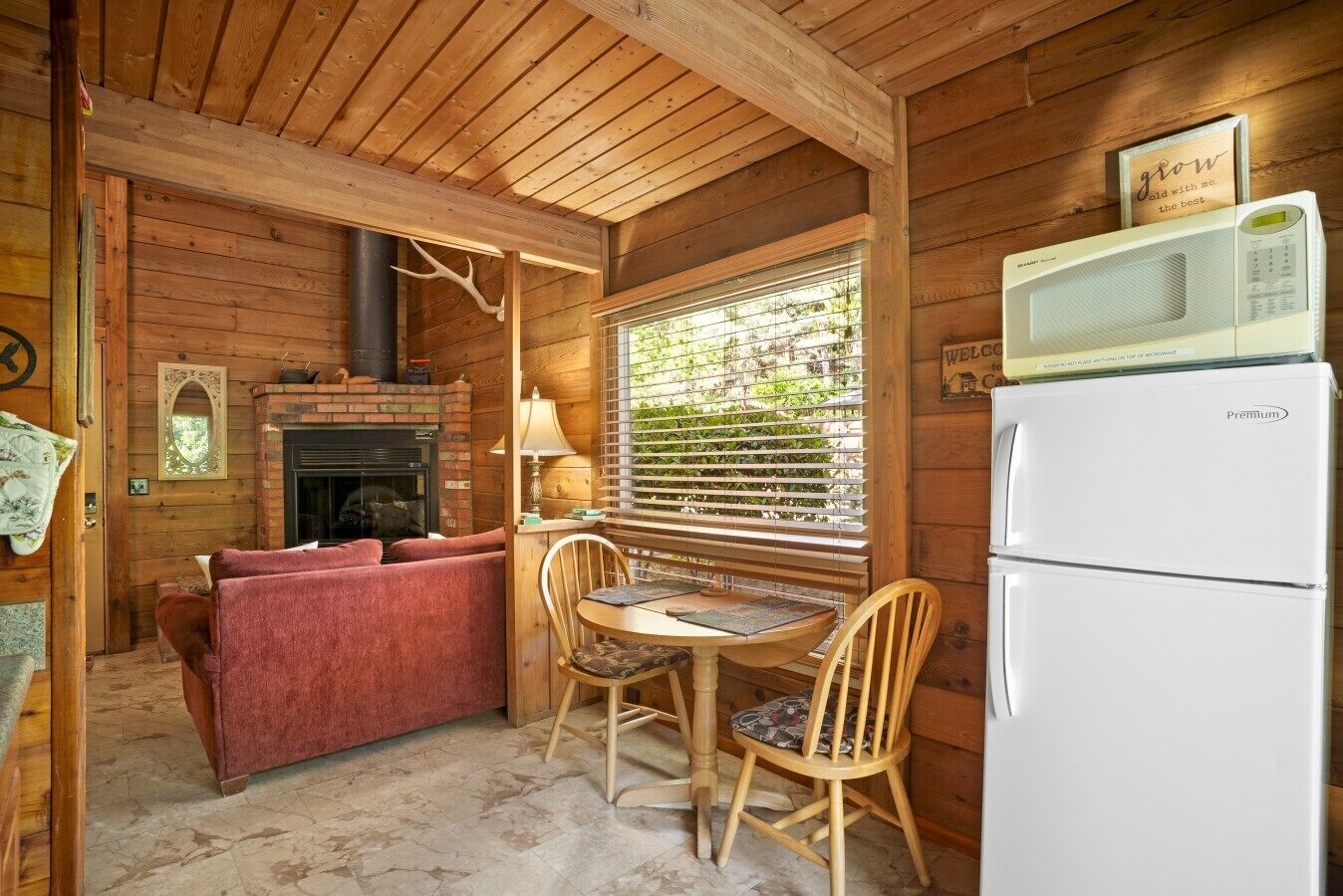 A cozy cabin interior with a fireplace, a dining table with chairs, a sofa, and a refrigerator.