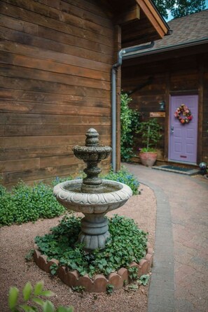 Une fontaine en pierre dans un jardin, avec un bâtiment en bois en arrière-plan.