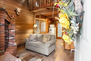 L'intérieur d'un chalet accueillant, avec une cheminée, un canapé agrémenté de coussins à motifs et une décoration murale.