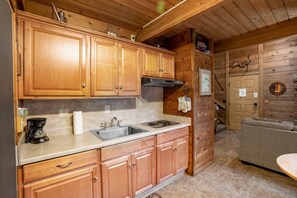 L’intérieur d’un chalet en bois comprend un coin cuisine, un canapé et une porte ornée de bois de cerf.