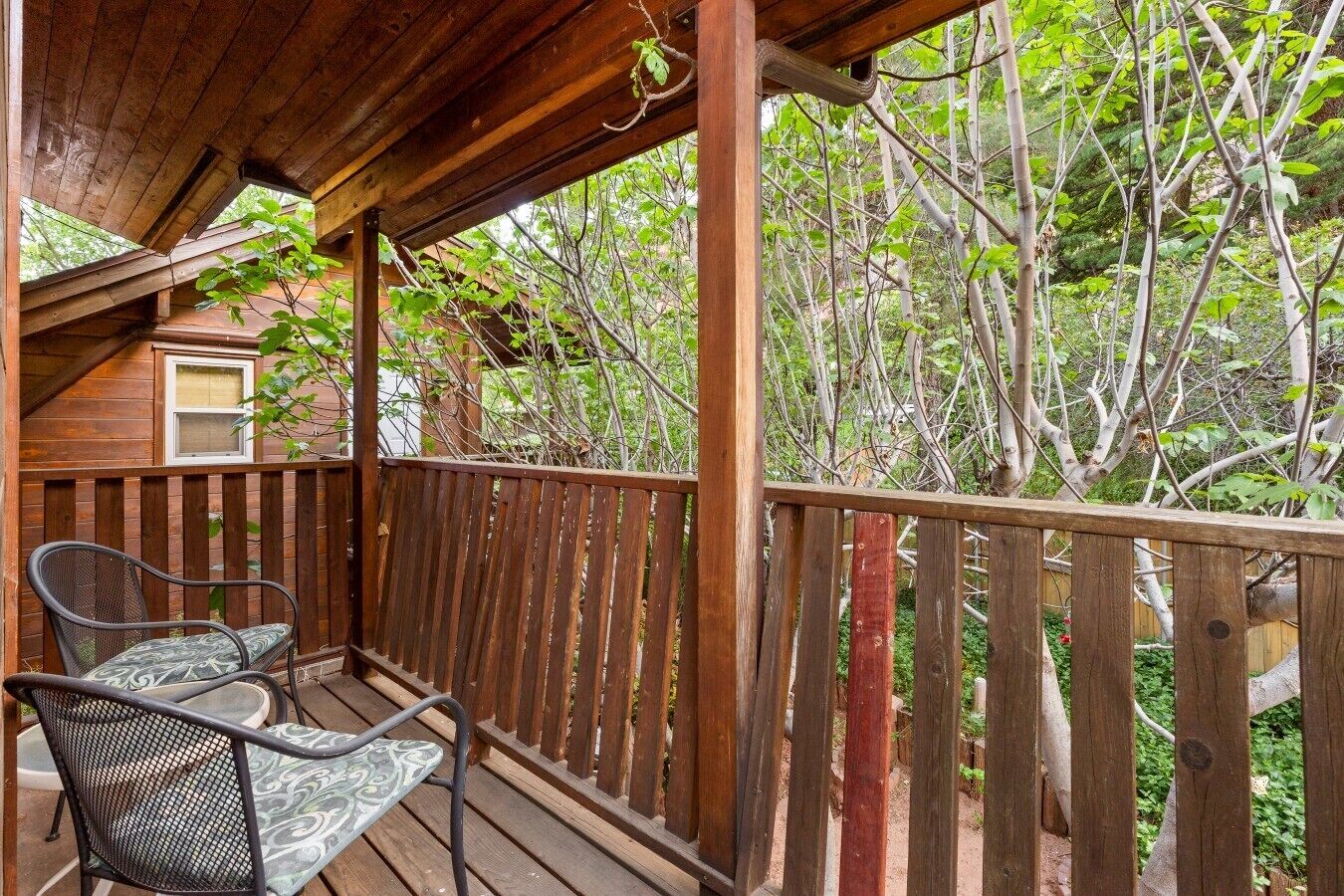 A wooden deck with two chairs and a table, surrounded by a wooden railing, overlooking a dense green forest.
